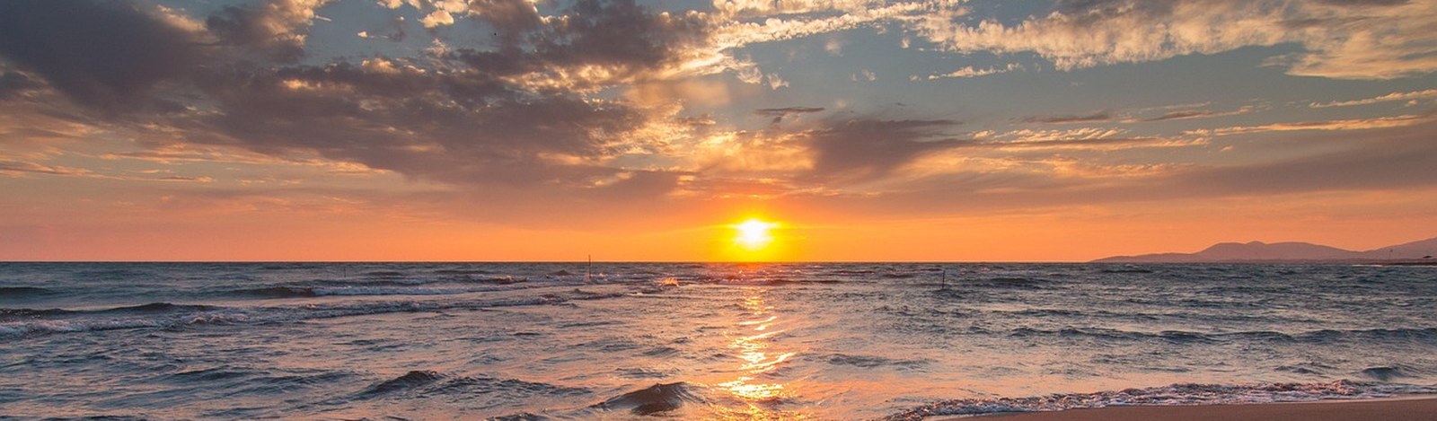 Ruhige Wellen am Strand im Sonnenuntergang, Licht spiegelt sich im Meer